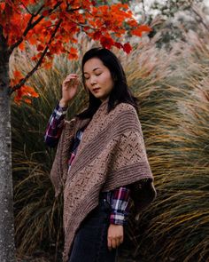 a woman standing in front of a tree with her eyes closed wearing a sweater and jeans