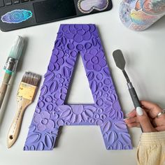 a person holding a paintbrush next to a purple letter