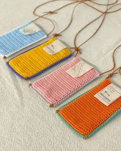 four crocheted bags with tags attached to them sitting on a white tablecloth