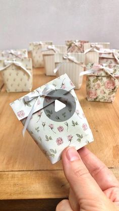 a person is pointing to a small gift box on a table with other boxes in the background