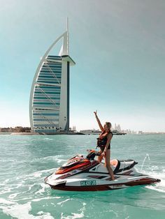 a woman riding on the back of a jet ski in the ocean next to a tall building