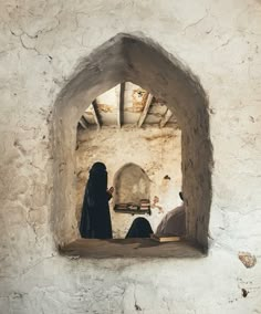 two people in black robes are sitting at a table and one person is looking out the window