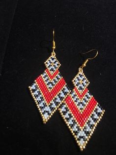 a pair of red, white and blue beaded earrings on a black surface with gold earwires