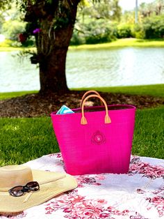 a bright pink bag sitting on top of a blanket next to a hat and sunglasses