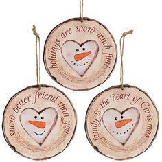 three wooden ornaments with snowman faces and words written on the front, two are hanging from twine strings