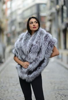 a woman standing in the middle of a street wearing a gray fur vest and black leggings