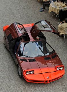 an orange sports car parked on the side of a road next to tables and chairs