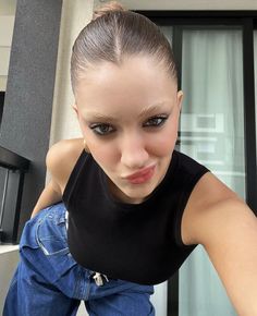 a young woman posing for the camera with her hair pulled back in a ponytail and blue jeans