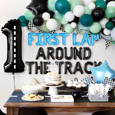 a first birthday party with balloons, cake and desserts on a table in front of a sign that says first lap around the track