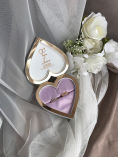 two heart shaped boxes sitting on top of a white cloth next to a bouquet of flowers