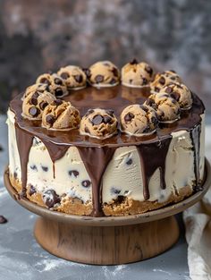 a cake with chocolate chip cookies and cream frosting on a wooden stand next to a white cloth