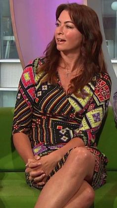 a woman sitting on top of a green couch in front of a tv screen with her legs crossed