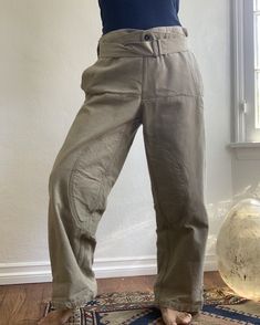 Subdued olive green canvas work pants. Padded legs, front buttons in a sailor style fashion, drop down front with “interior” front pockets, buckle cinch at leg hems and waist. Note: Openings at side “pockets” as these are intended as over pants. See photo. Fabric: CanvasFit: M|L up to 34 inches Measurements (flat): Waist 17 inches (can adjust smaller) Hips 19.5 inches Rise 13.5 inches Inseam 28.5 inches Length 40.5 inches Leg opening 9.75 inches Condition: Excellent Military Style High Waist Parachute Pants In Khaki, Military Style High Waist Khaki Parachute Pants, Olive Cargo Style Workwear Bottoms, Olive Cargo Style Bottoms For Work, Khaki High-waisted Utility Parachute Pants, Utility Parachute Pants With Belt Loops In Khaki, Fitted Khaki Utility Parachute Pants, Olive Military Cargo Pants, Olive Utility Bottoms For Outdoor