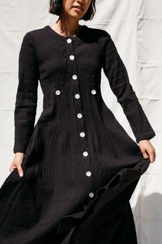 Long-sleeved, calf-length dress with shell buttons down the front and tabs at waist. Relaxed fit Side pockets 98% Cotton 2% Spandex. Made in India. An is 5'7” and wears size 2. Black Cotton Shirt Dress With Buttons, Vintage Fashion Black Buttoned Dresses, Black Cotton Smocked Dress With Ruched Detail, Black Button-up Dress With Buttons, Black Vintage Button-up Dress, Crinkle Fabric, Calf Length Dress, Woman Dress, Shell Buttons