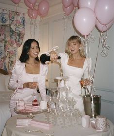 two women sitting at a table with pink balloons