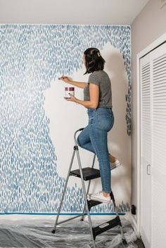 a woman is painting a wall with blue and white designs on it, while she stands on a ladder