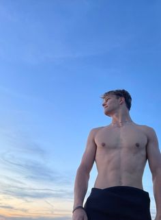 a shirtless man standing on the beach at sunset