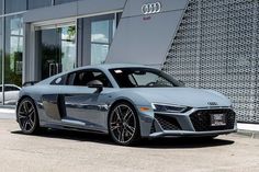 a grey audi sports car parked in front of a building with large windows and doors