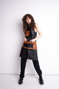 a woman wearing a black and brown leather apron, standing in front of a white wall