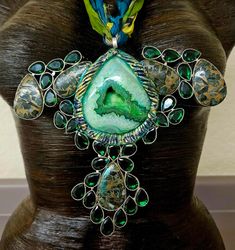 This piece is a combination of an upcycled necklace I never wore, along with a luxury green druzy agate teardrop cabochon I set into hand sculpted material. The end result looks somewhat like an Avant Garde Crucifix, ala Madonna! I believe the green stones are just faceted and cut glass, and I cannot recall what the other mosiac stones are. I painted the sculpted material in a variety of paints then sealed it with a high gloss glaze to protect the finish. The lightweight and comfortable pendant is support by five strands of distressed sari silk which I simply tied in a bow in the back. Shown here at a length of 24" and you can adjust accordingly. OOAK Wearable Art from the Atelier of Kat Kouture! Upcycled Necklace, Sculpting Materials, Luxury Green, Jewellery Shop Design, Turquoise Western, Green Stones, Chest Piece, Sari Silk, Western Jewelry