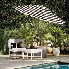 an umbrella and chair next to a swimming pool with plants in the backgroud