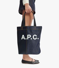 - Unisex model. - Tote bag in Japanese denim. - Two large handles to carry the bag by hand or on the shoulder. - Reinforced base. - Interior zip pocket. - Large A.P.C. logo on the front. - Caramel topstitching on the denim. Faux Leather Bag, Exclusive Clothing, C Logo, Japanese Denim, Backpack Tote Bag, Support Team, Dark Navy Blue, Scarf Jewelry, Tote Backpack