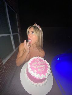 a woman sitting in front of a pink birthday cake