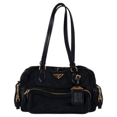 This 100% authentic Prada bowling bag is crafted from black nylon and features black leather trim, offering a sleek and functional design. It includes three zipper pockets and a flap pocket on the outside for easy access, along with a luggage tag and the signature triangle logo patch. The bag closes with a two-way zipper on top and is lined in logo nylon with a zipper pocket against the back, providing ample storage and organization. This Prada bowling bag combines style and practicality, perfect for everyday wear. Has been carried with slight wear to the bottom corners. Overall in excellent condition. Comes with authenticity card and dust bag. Measurements Model BR2521 Height 18cm (7in) Width 28cm (10.9in) Depth 12cm (4.7in) Drop of the Handle 23cm (9in) Hardware Gold-Tone All our listing Designer Nylon Bag With Double Handle, Prada Bowling Bag, Black Nylon Bags With Leather Handles, Black Nylon Bag With Zipper Pocket, Prada Nylon Handbags, Bag With Pockets, Bowling Bag, Bowling Bags, In Logo