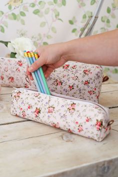 two pencils are being held in front of a flowered bag on a table