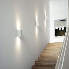 three lights are on the wall next to some stairs in a room with white walls