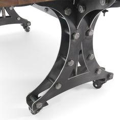 an iron and wood dining table with wheels on the legs, against a white background