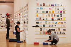 two people looking at pictures on the wall in an art gallery, while another person sits on the floor