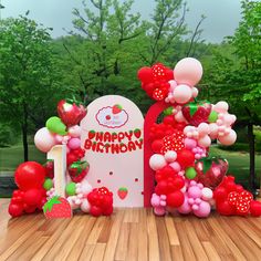 a happy birthday sign made out of balloons and strawberries on a wooden table with trees in the background