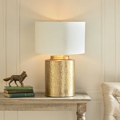 a table with a lamp, books and a cat figurine sitting on it