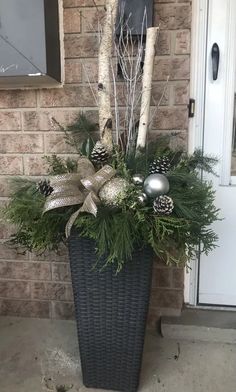 a basket filled with pine cones and greenery next to a brick wall in front of a door