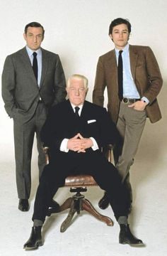 three men in suits and ties posing for a photo with one sitting on a chair