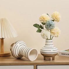 a white vase with flowers sitting on a table next to a lamp and some books