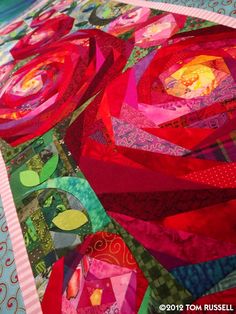 a close up of a quilt on a bed with red and pink flowers in the center