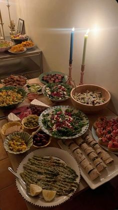 a table filled with lots of food on plates next to a lit candle and candlestick