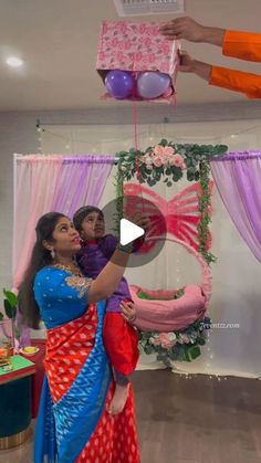 two women dressed in colorful sari are holding up a pink and blue gift box