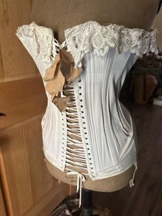 This is a beautiful antique French corset made from a white striped  cotton with a beautiful lace trim and silk bow. I have had it on a dress form here for years but I'm redoing things and parting with it . I actually paid more than I'm asking for it - but I just had to have it . The total width is about 30" and 19" high, of course the width can be adjusted . It's in very good condition with one small spot and some tarnishing on the garters . They are getting harder to find and this one is lovely. White Victorian Wedding Corset, Victorian White Underbust Corset, White Fitted Corset With Lace Trim, White Underbust Bodice With Lace Trim, White Victorian Overbust Corset, White Historical Design Corset For Wedding, White Boned Bodice Corset For Costume, White Cotton Corset Dress With Corset Back, Historical Design White Wedding Corset