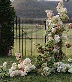 an arrangement of white and pink flowers in front of a black iron fence with hills in the background