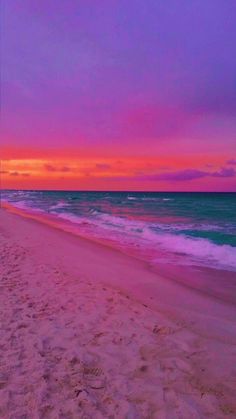 the beach is pink and blue with waves coming in