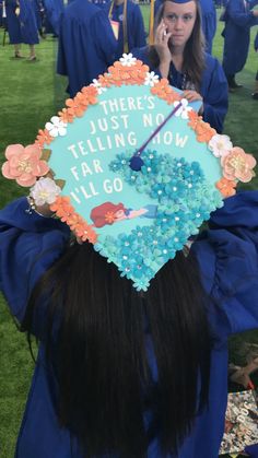 a woman wearing a blue graduation cap with flowers and writing on it, while talking on her cell phone