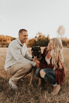 a man and woman sitting in the grass with their dog