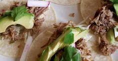 three tacos with meat, lettuce and avocado on them sitting on a plate