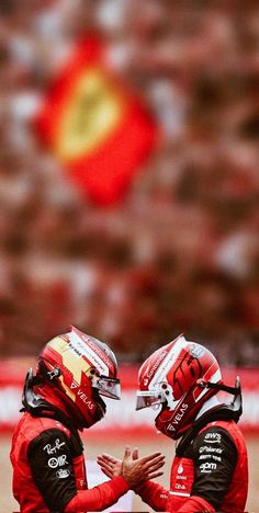 two men in racing gear sitting on the ground with their hands together and looking at each other