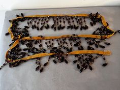 two pieces of jewelry sitting on top of a metal pan covered in black beads and yellow ribbon