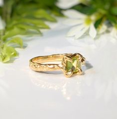 Show your love with this exquisite Peridot ring. Handcrafted in wax and cast in Solid 14k Gold, this stunning green crystal ring features an organic textured band, ensuring its uniqueness. Adorned with a mesmerizing princess-cut Peridot, also the August birthstone, it embodies more than an engagement ring - it symbolizes timeless love and individualityT H E ∙ S M A L L ∙ D E T A I L S• Princess-cut Peridot (5 x 5mm)• Solid 14k Gold textured bandM A T E R I A L ∙ O P T I O N S• Sterling Silver• S Organic Gold Engagement Ring, Peridot And Diamond Engagement Rings, Green Open Ring For Promise, Elegant Green Citrine Jewelry, Elegant Green Jewelry In Recycled Gold, Fine Green Citrine Jewelry, Green Crystal Promise Ring In Fine Jewelry Style, Fine Jewelry Peridot Rings For May Birthstone, Emerald Cut Peridot Gemstone Jewelry