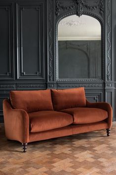 an orange couch sitting in front of a mirror on a wooden floor next to a black wall